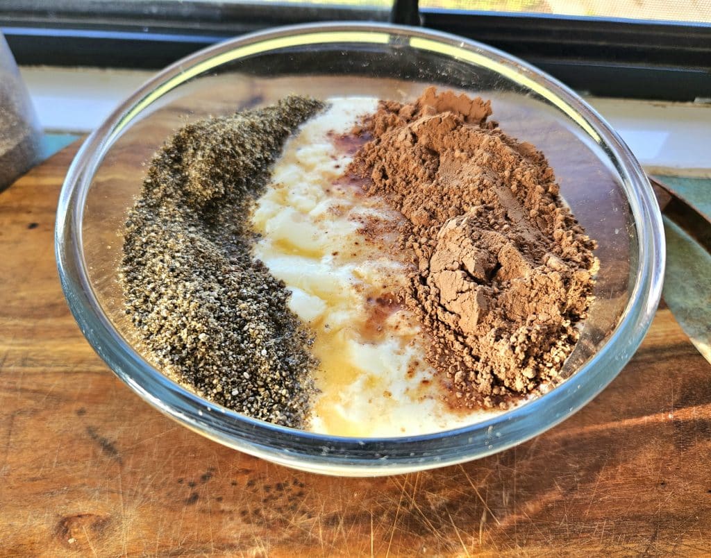 Kefir milk in bowl on the bench. Blended chia seeds, rapadura sugar and cacao powder on top of it.