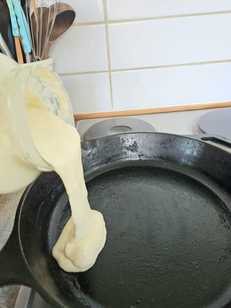 Sourdough discard being poured into a hot cast iron pan.