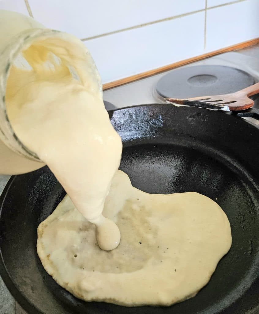 Sourdough discard being poured into a hot cast iron pan. Starting to form sourdough pizza crust.