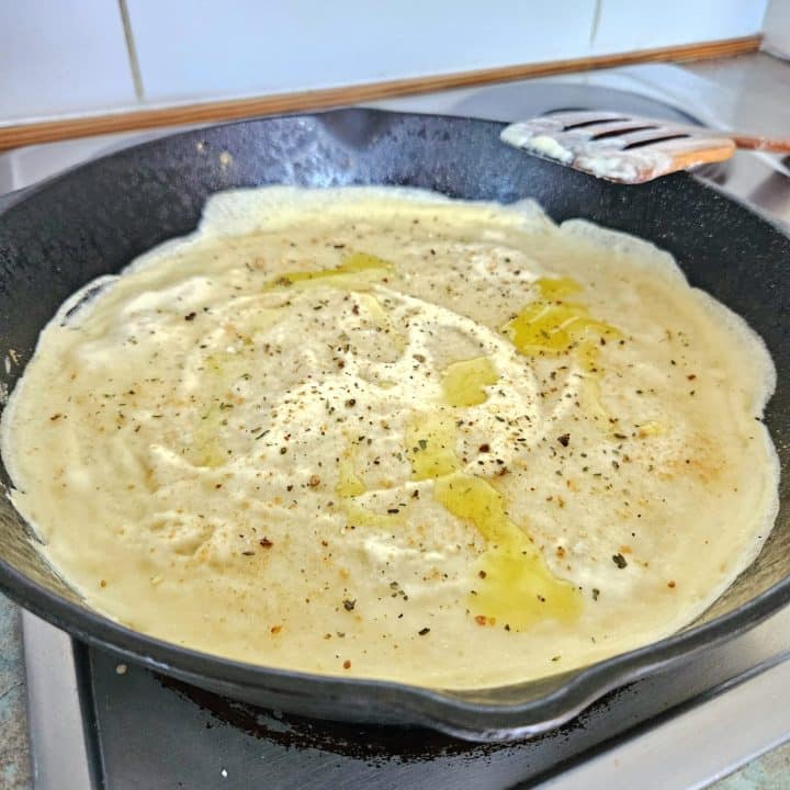 Sourdough discard spread onto a cast iron pan topped with sea salt, Italian seasoning and olive oil.