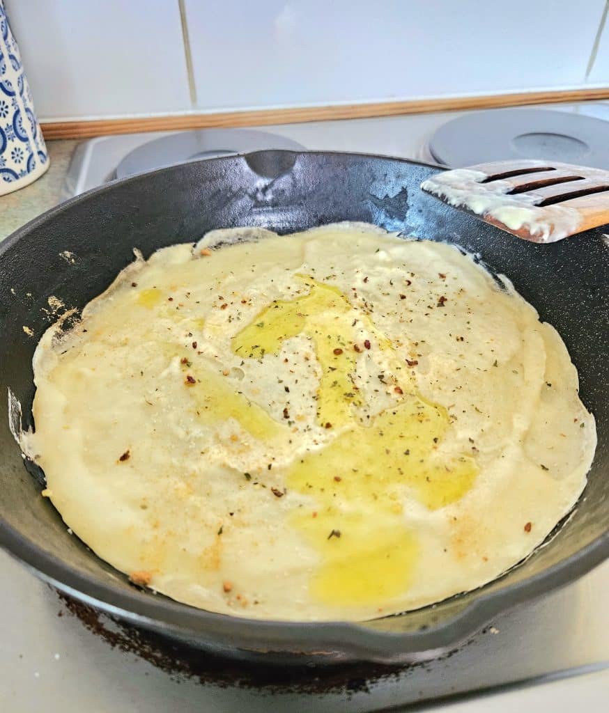 Sourdough discard spread on a cast iron pan sprinkled with salt, Italian seasoning and olive oil.