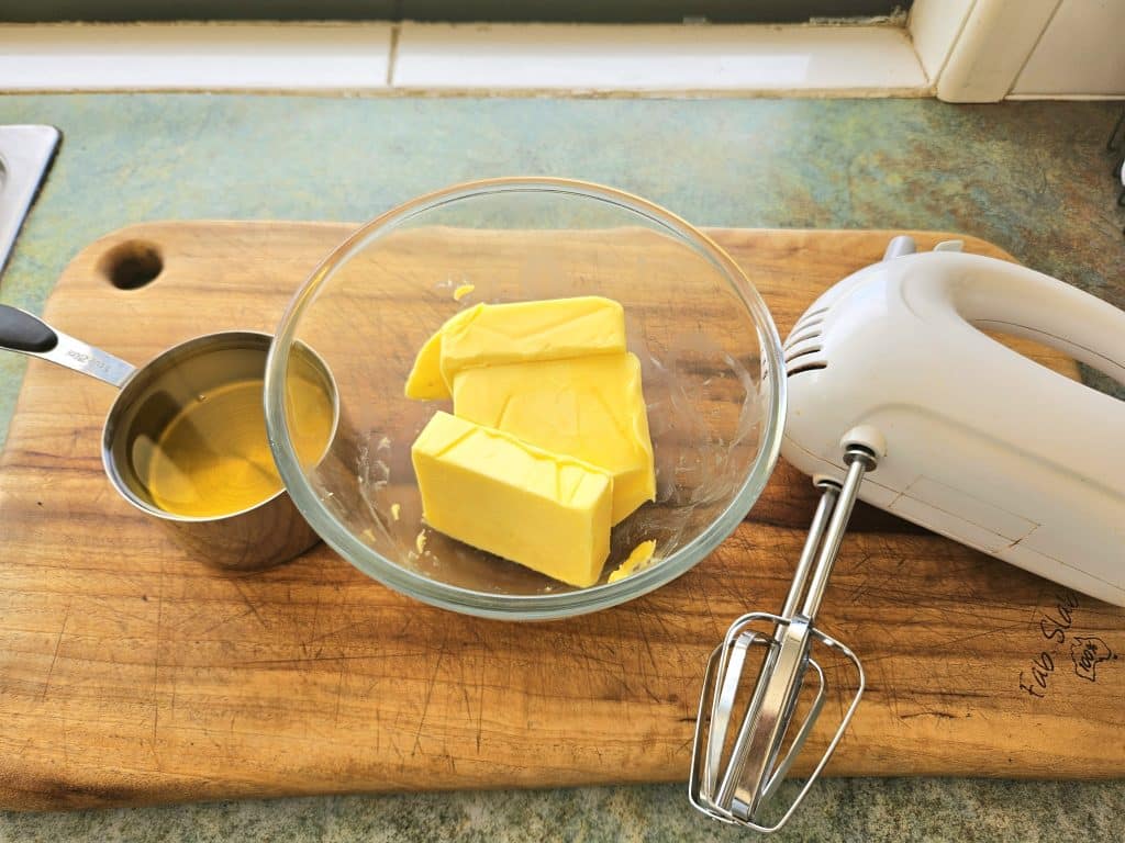 Butter, oil and a handheld whisk on a cutting board.