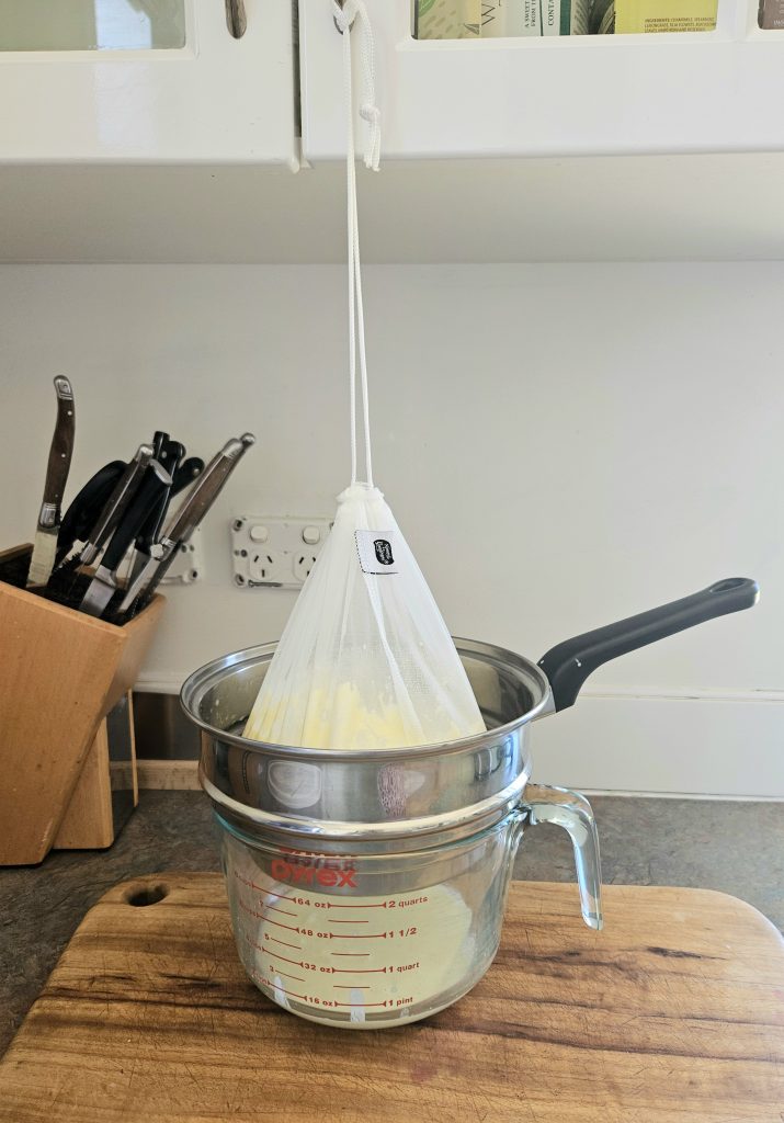 Milk kefir hanging from a milk bag. Whey being strained out onto a large measuring glass.