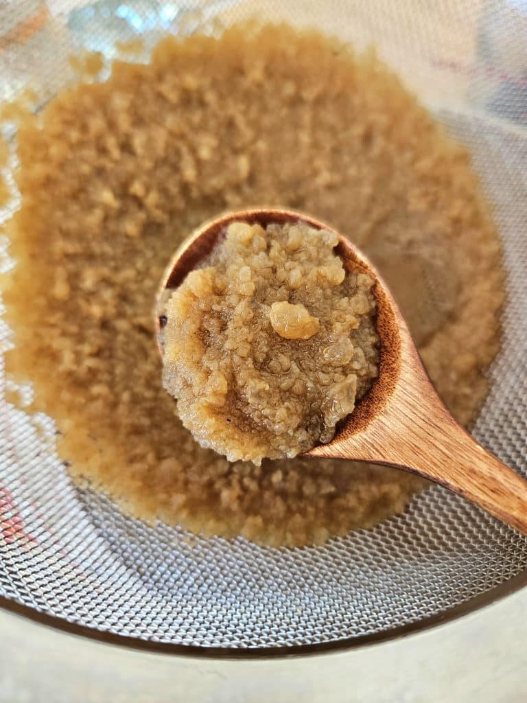 water kefir grains being strained in a mesh strainer. Grains on a wooden spoon.