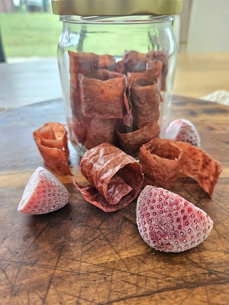 Scoby Fruit leather on a cutting board with strawberries.