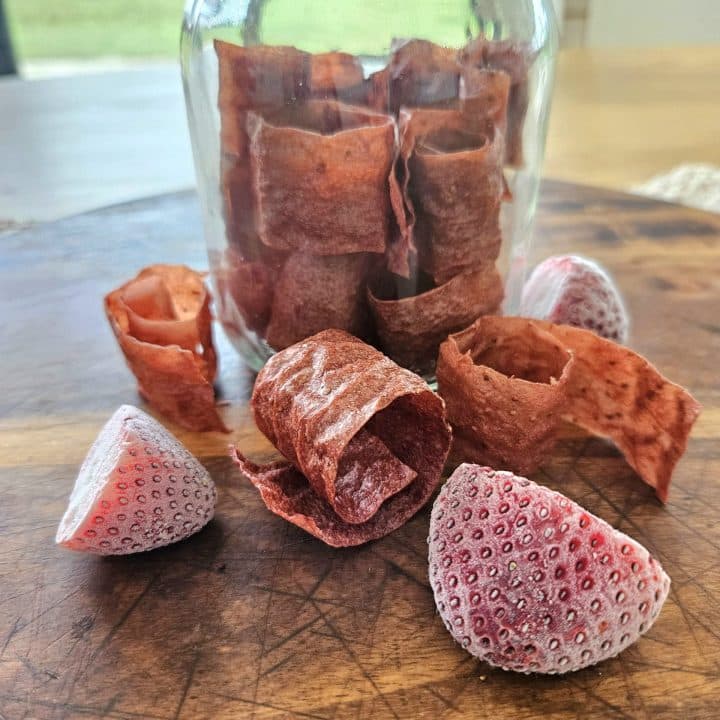 Scoby Fruit leather on a cutting board with strawberries.