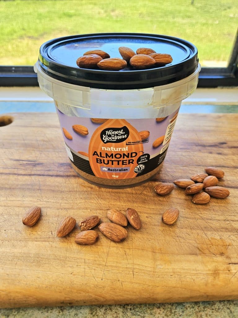 Almond butter with almonds surrounding it on a cutting board.