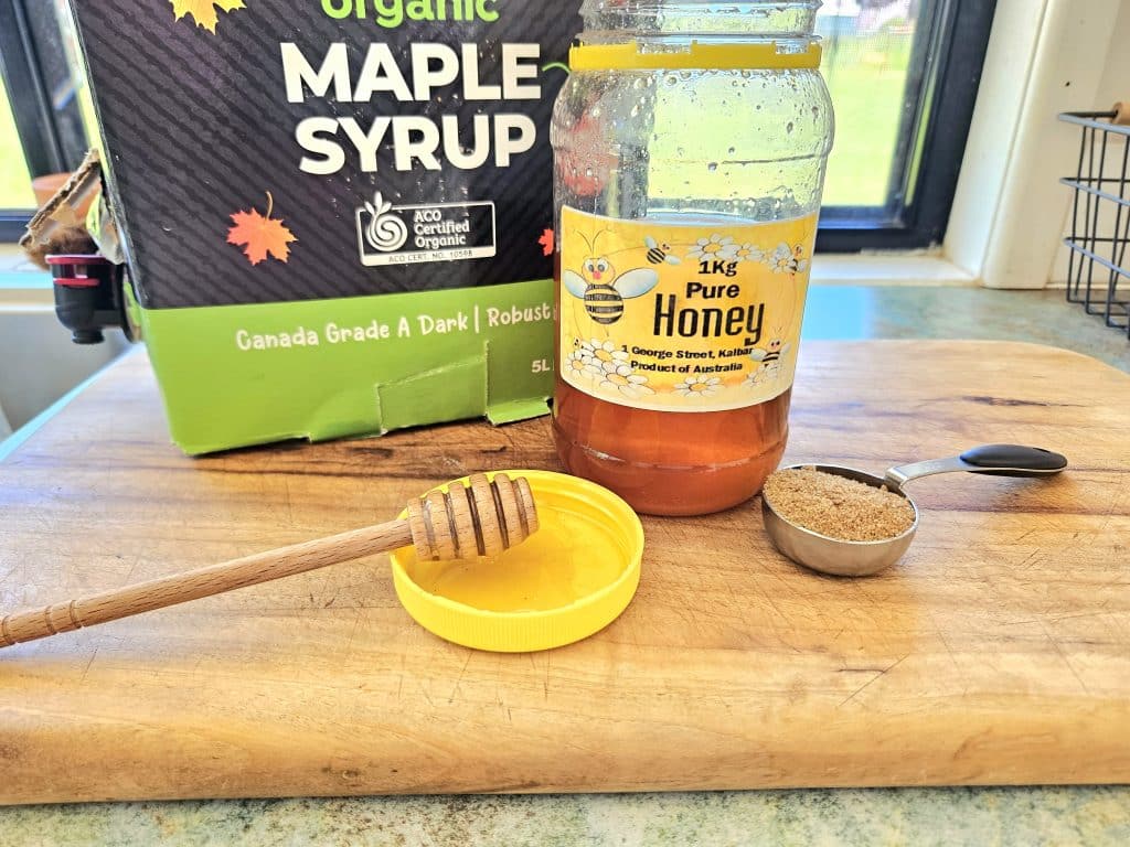 Honey, Maple syrup, Rapadura sugar displayed on a cutting board in the kitchen. Simple pantry food swaps.