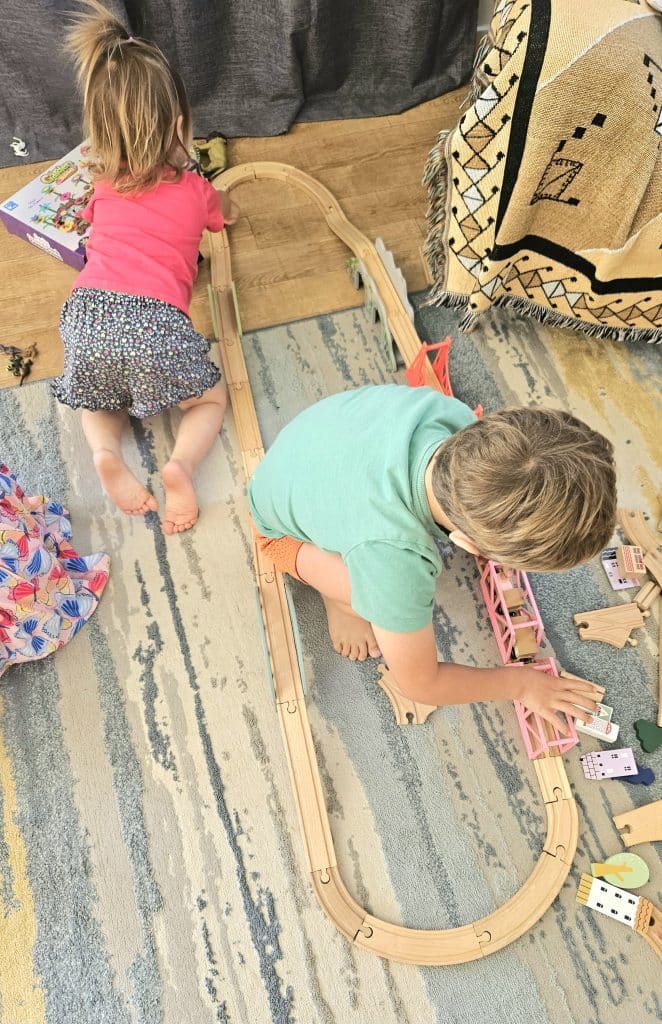 Kids playing on a rug with a train set.