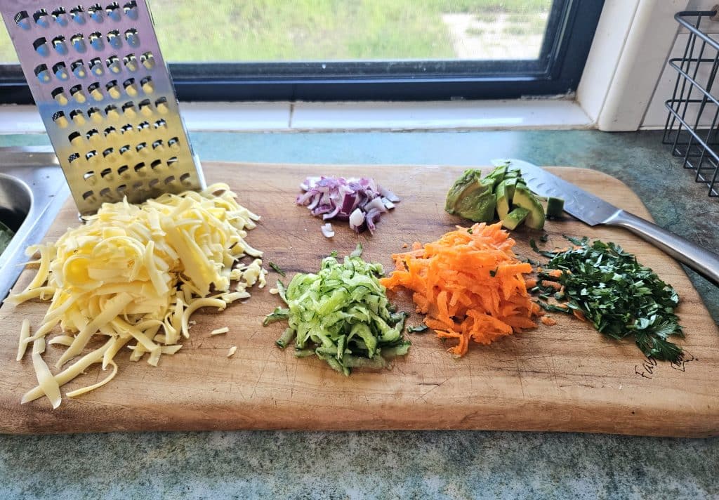 Traditional wife prepping food for dinner. Shredded cheese, carrot, cucumber and onion on a cutting board on the kitchen bench.