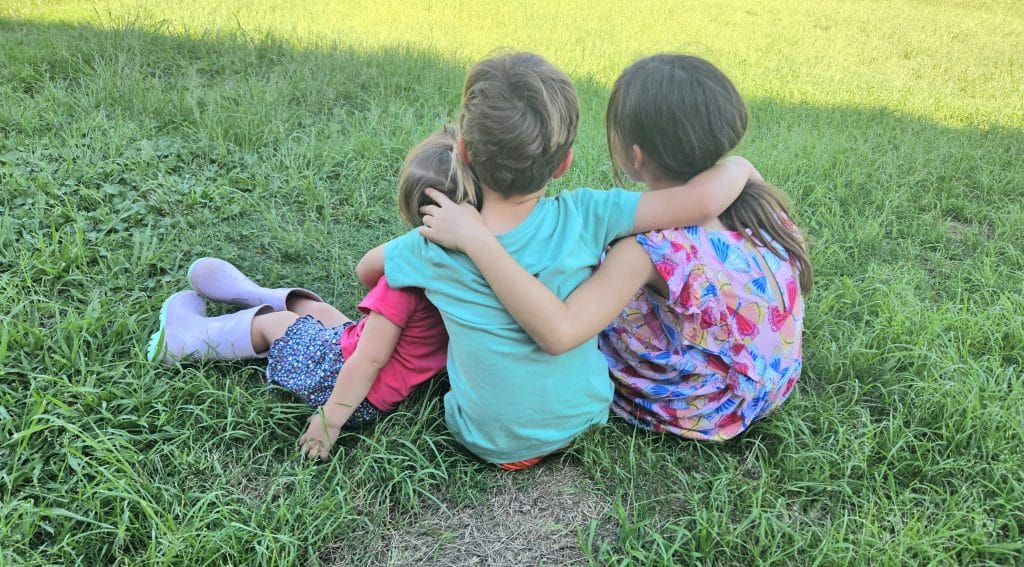 kids sitting on the grass hugging each other.