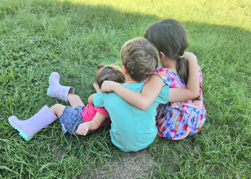 kids sitting on grass hugging each other.