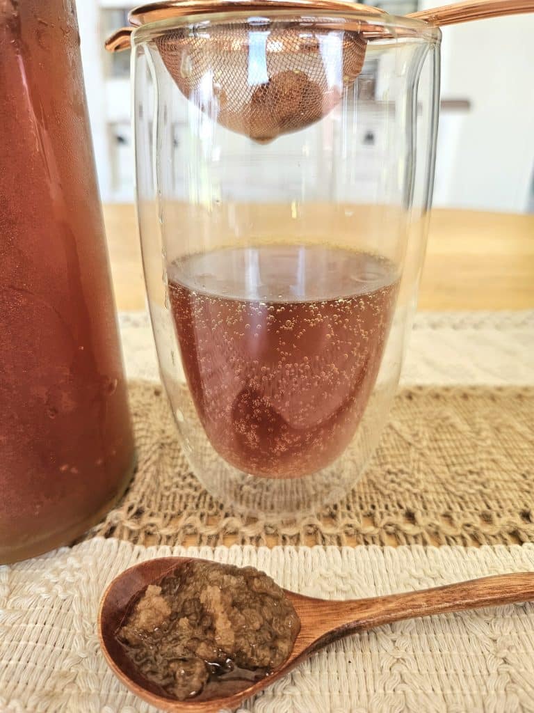 water kefir soda being strained into a cup. water kefir grains on a table.