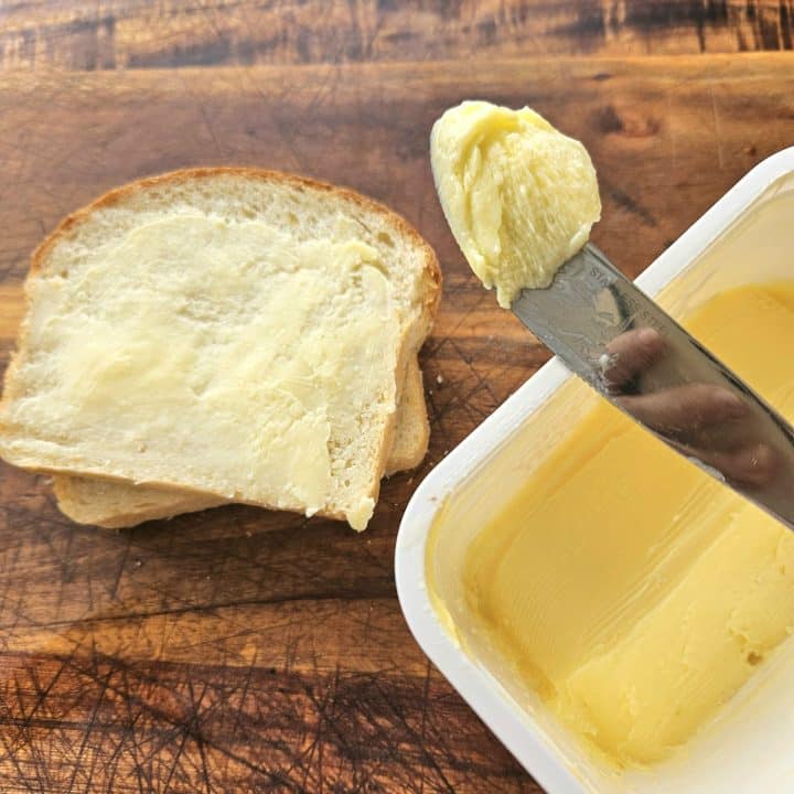 Spreadable butter on a knife, in a container and on a piece of toast.