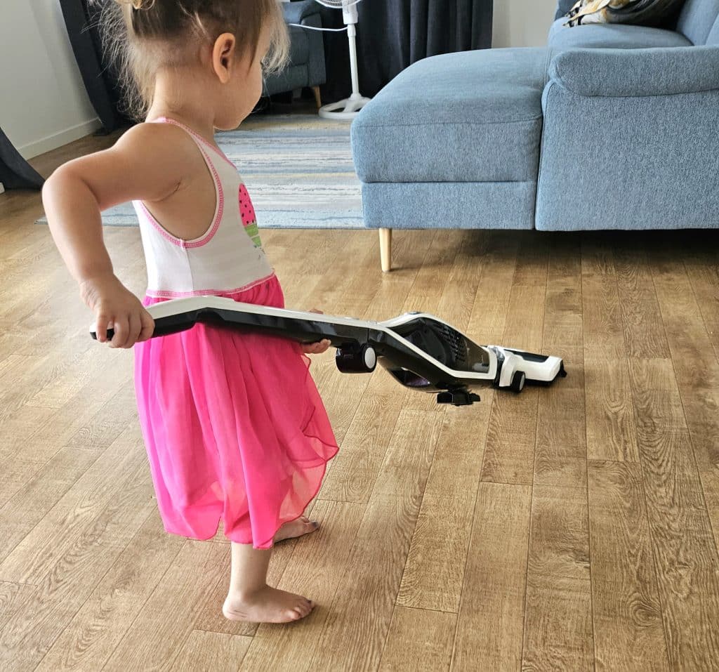 Toddler vacuuming floors with handheld vacuum.