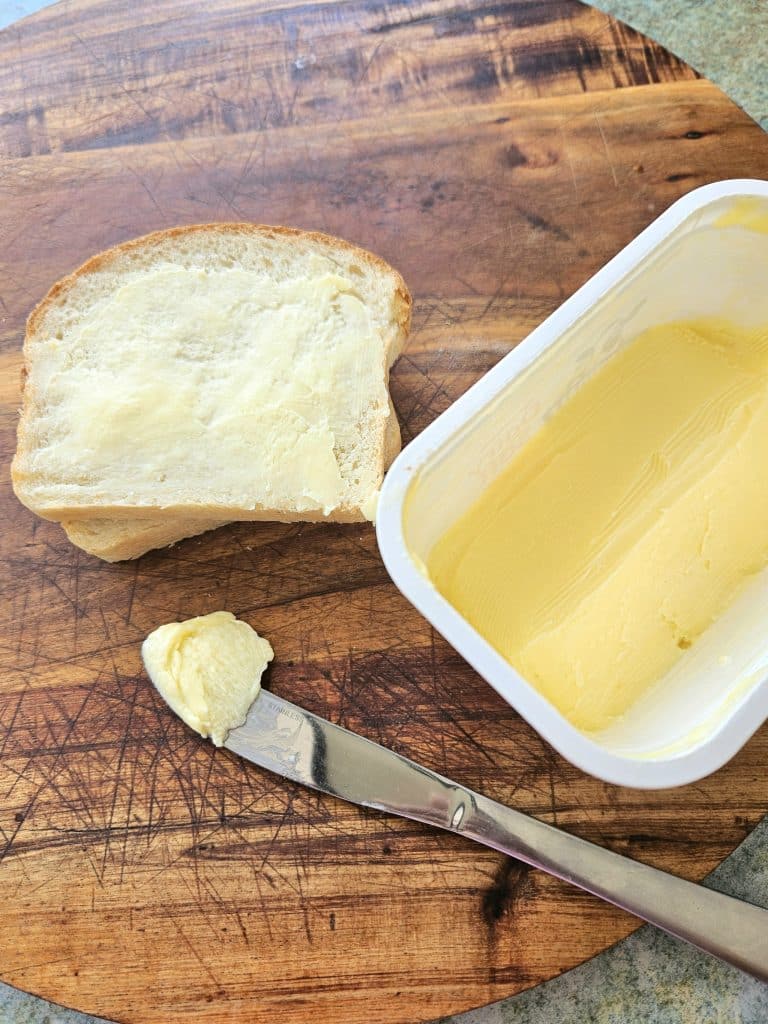 Spreadable butter on a knife, in a container and on a piece of toast.