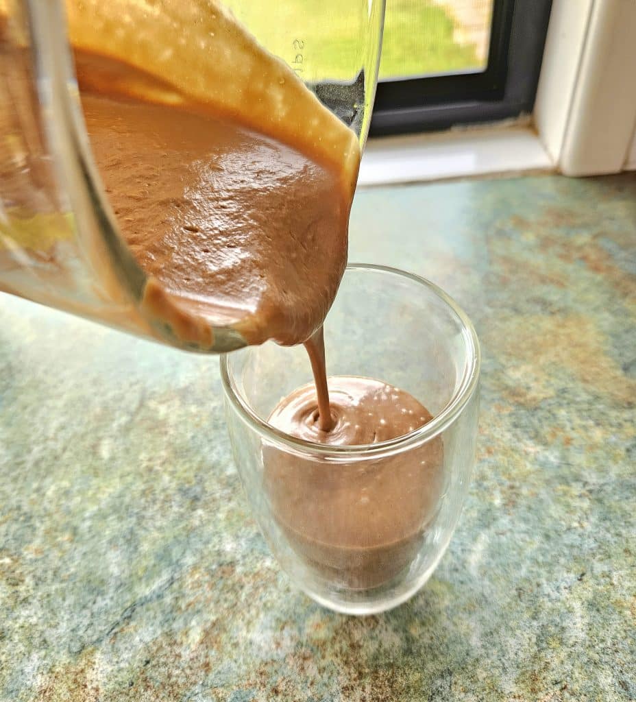 Creamy chocolate avocado smoothie being poured into a cup.