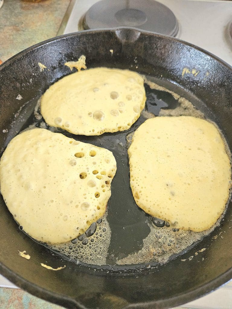 Sourdough Pancakes cooking in a cast iron pan.