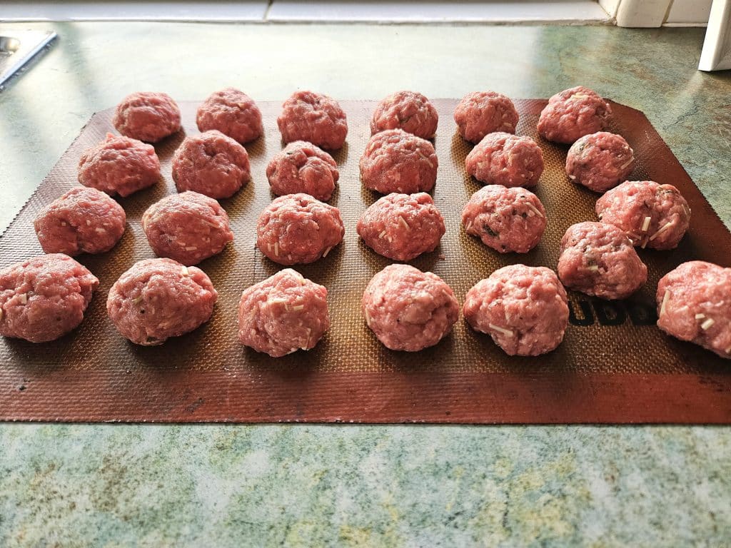 Homemade meatballs rolled up and ready to bake on a silicone mat.