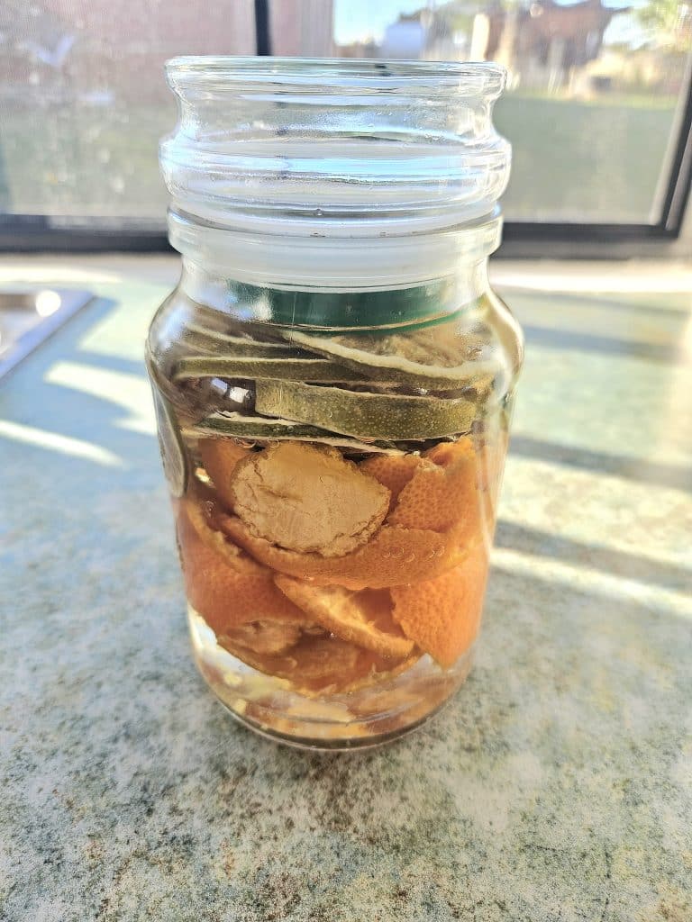 Citrus peels soaking in vinegar in a glass jar.