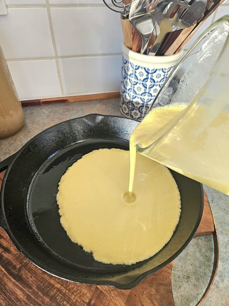 Pouring Dutch pancake mixture into a hot cast iron pan.