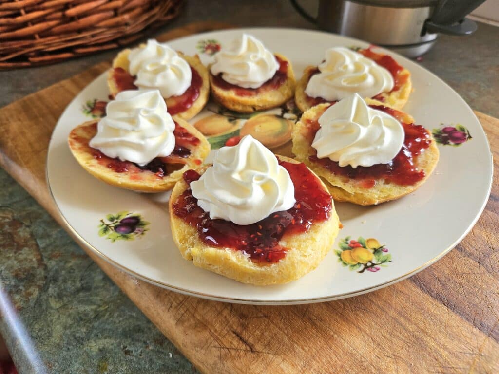 Homemade sourdough scones topped with jam and cream on a plate.