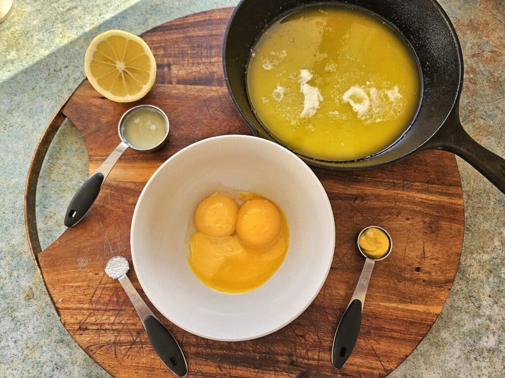 Hollandaise sauce ingredients on a cutting board. Eggs, melted butter, mustard, salt and lemon juice.