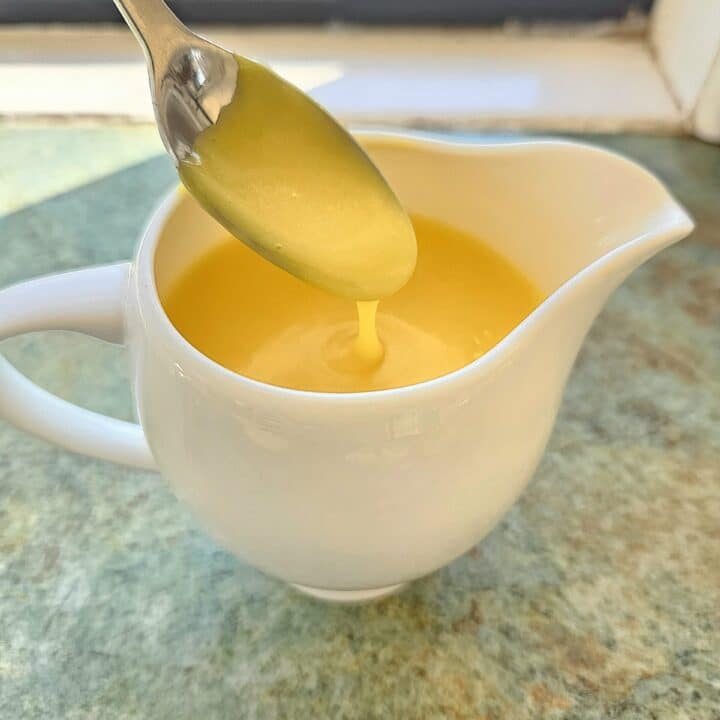 Hollandaise sauce in a jug being scooped in a spoon.