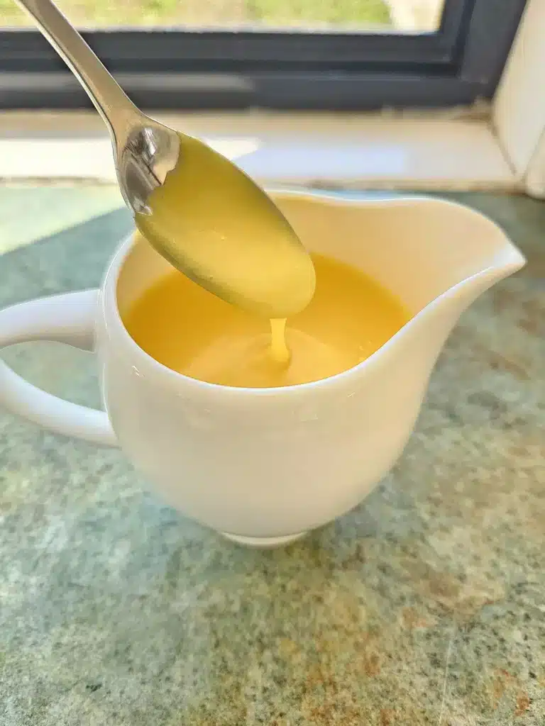 Hollandaise sauce in a jug being scooped in a spoon.