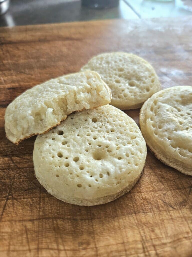 Soft sourdough crumpets resting on a cutting board.