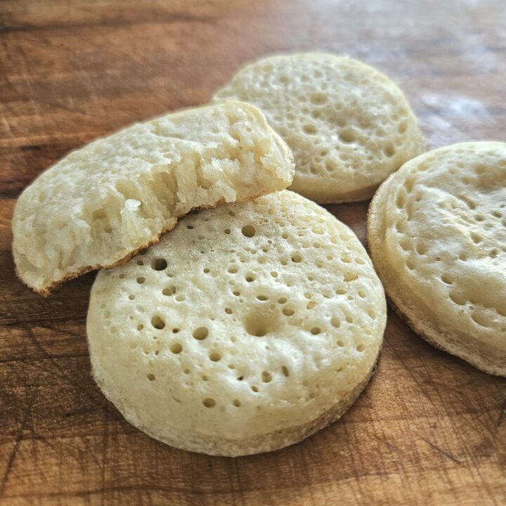 Soft sourdough crumpets resting on a cutting board.