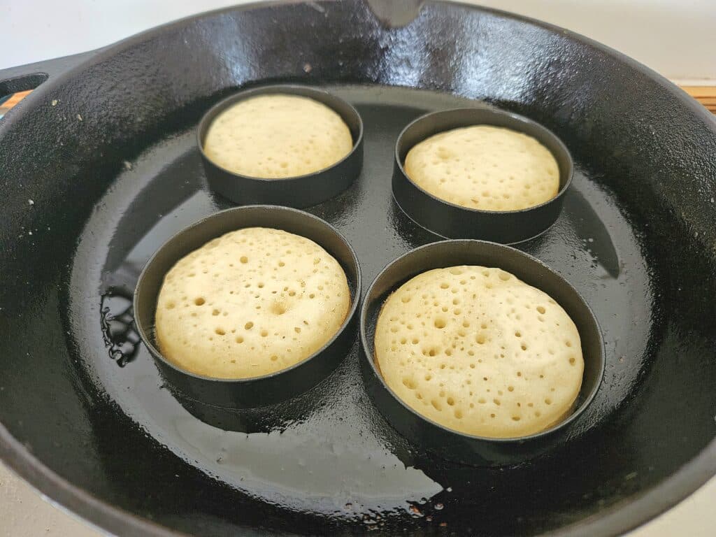 Sourdough crumpets cooking on a cast iron pan.