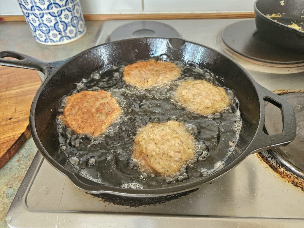 tuna fritters frying in a cast iron pan.