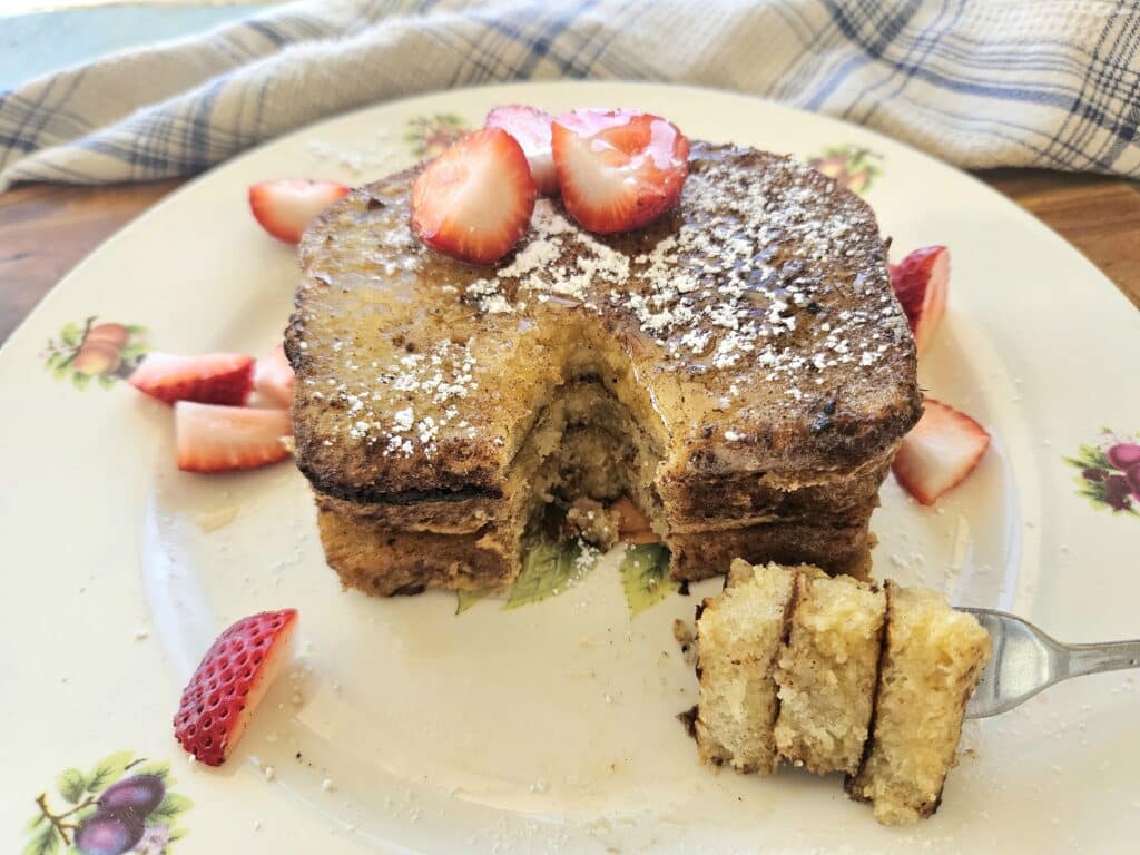 Sourdough French toast on a plate topped with strawberries and powdered sugar.