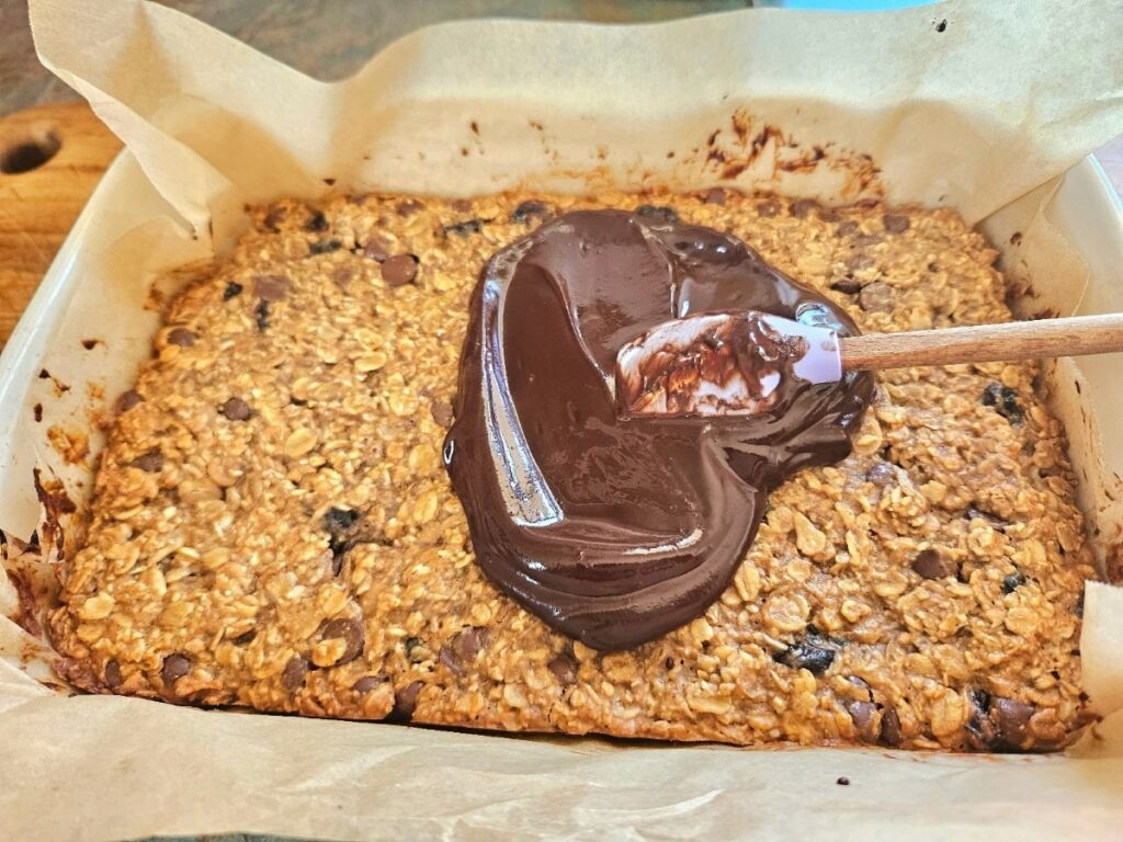 Spreading dark chocolate on top of granola bars.