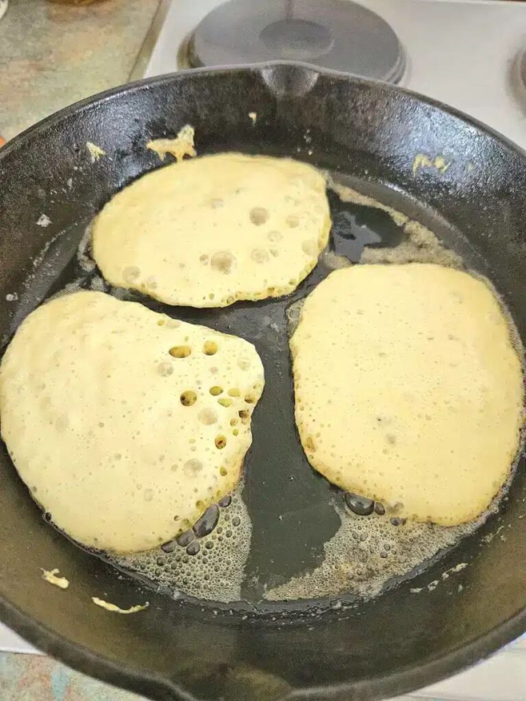 sourdough discard pancakes cooking in a cast iron pan.