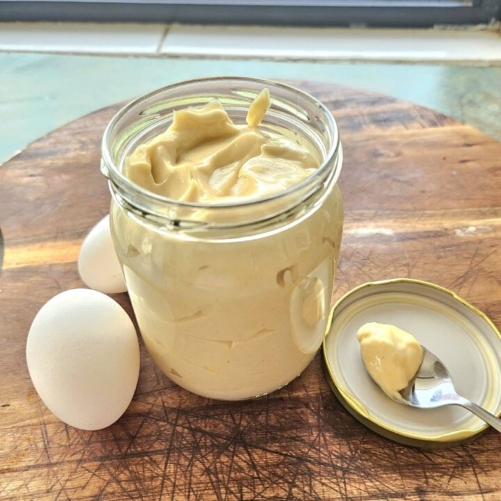 Creamy homemade mayonnaise in a container on a cutting board.