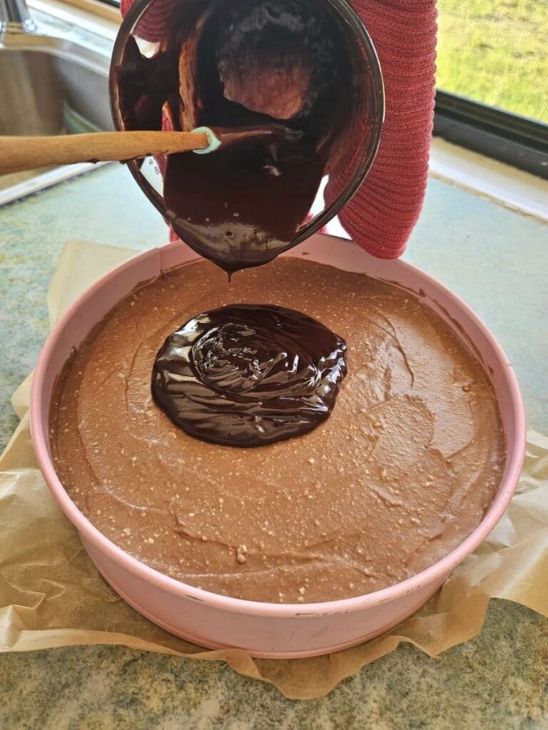 Pouring chocolate ganache on top of cheesecake.