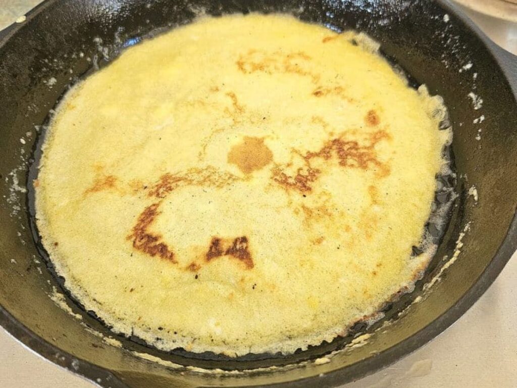 Cooking sourdough crepes in a cast iron pan.