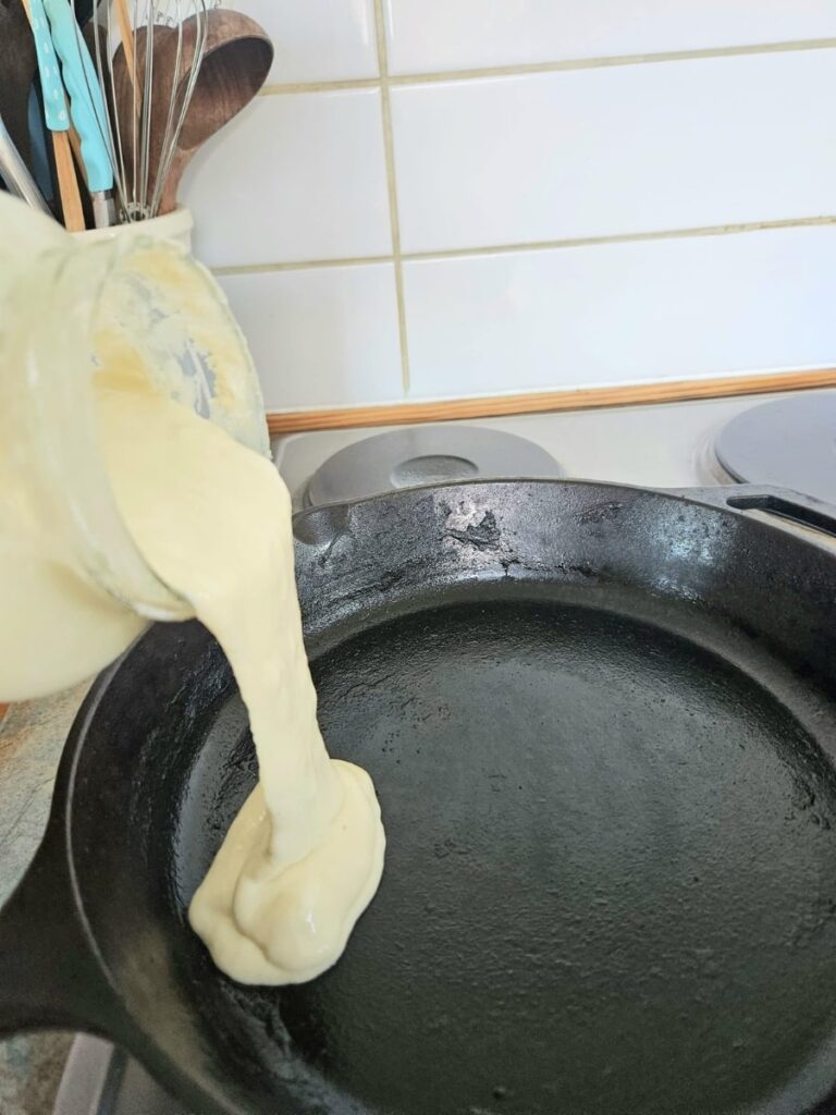 Pouring sourdough discard into hot cast iron pan.