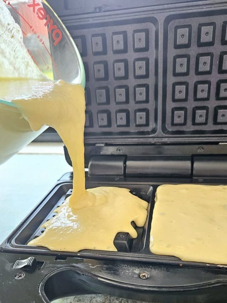 Pouring sourdough waffle batter into a waffle maker.