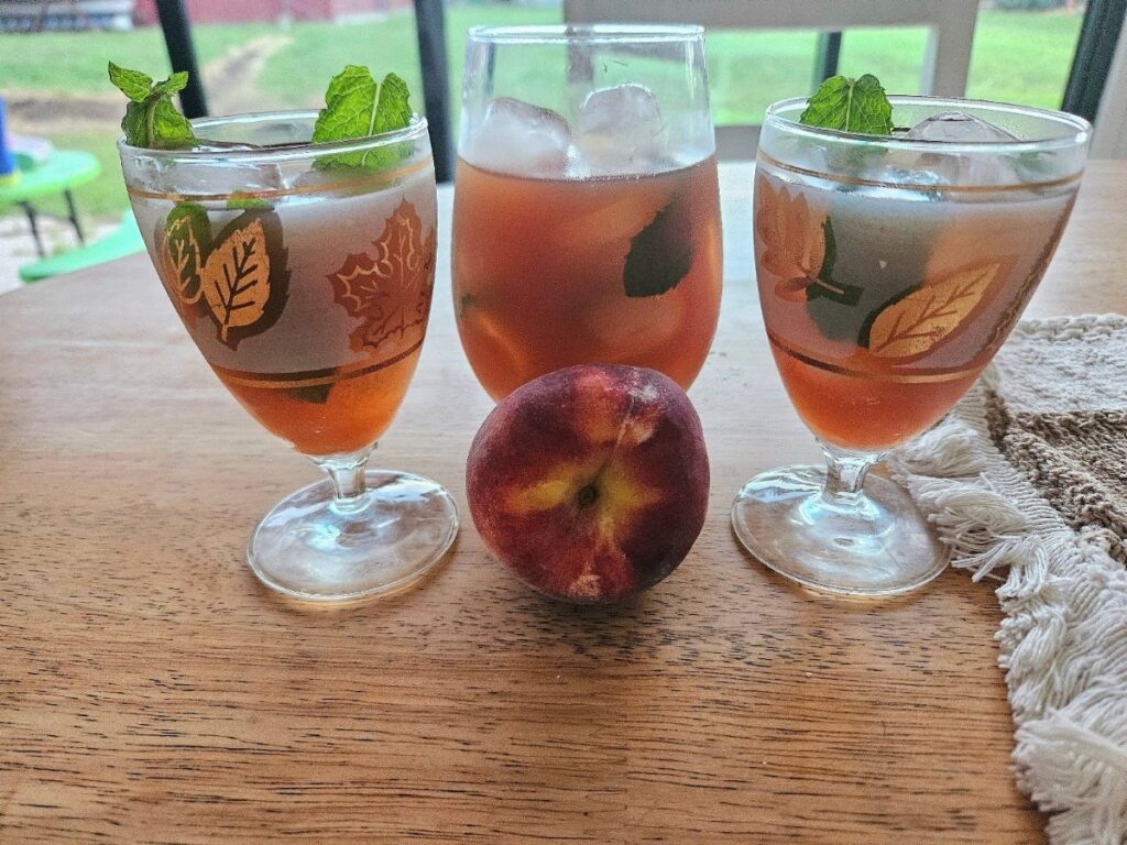 Homemade peach iced tea poured into 3 glasses on a table.