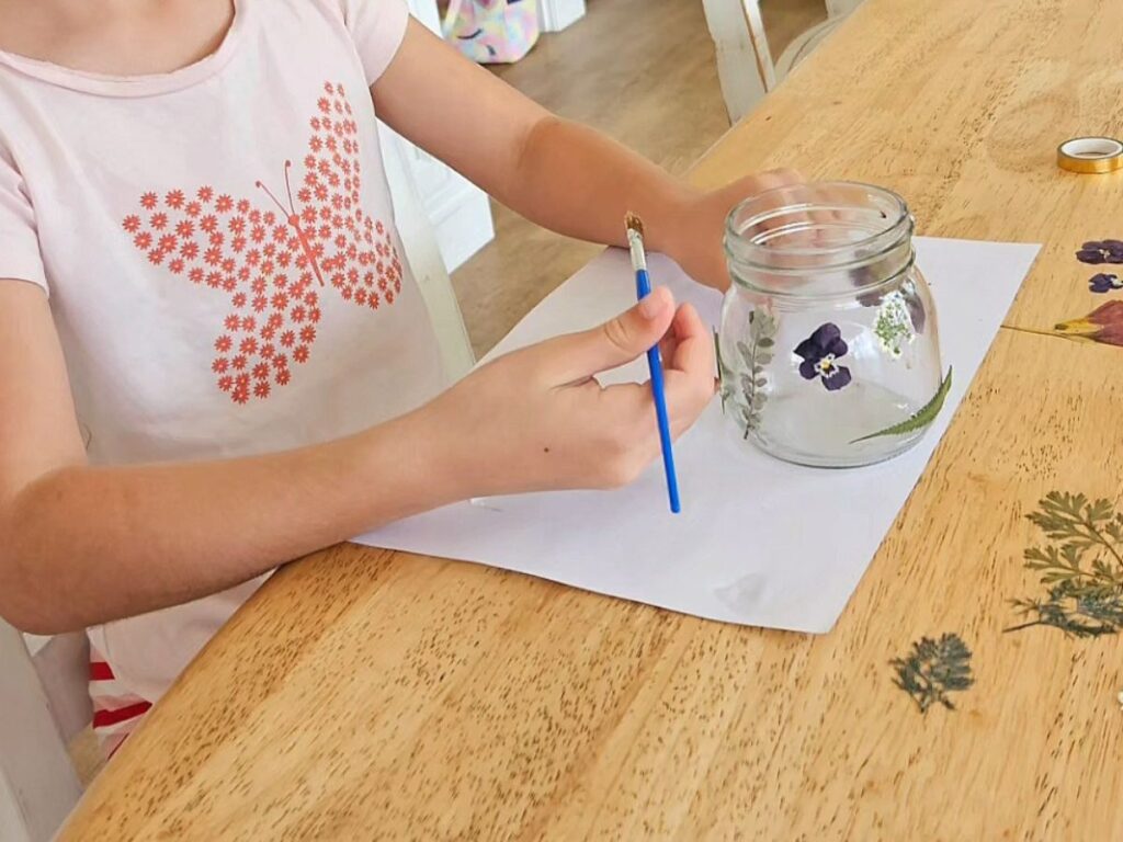 Glueing flowers to a glass jar.