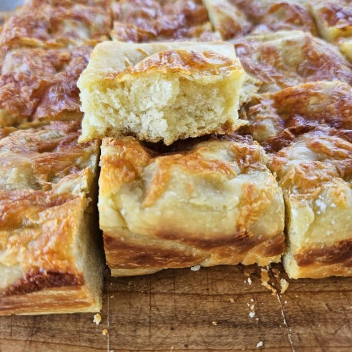 Soft and crunchy cheesy sourdough foaccia sliced on a cutting board.