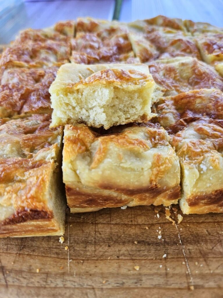 Soft and crunchy cheesy sourdough foaccia sliced on a cutting board.