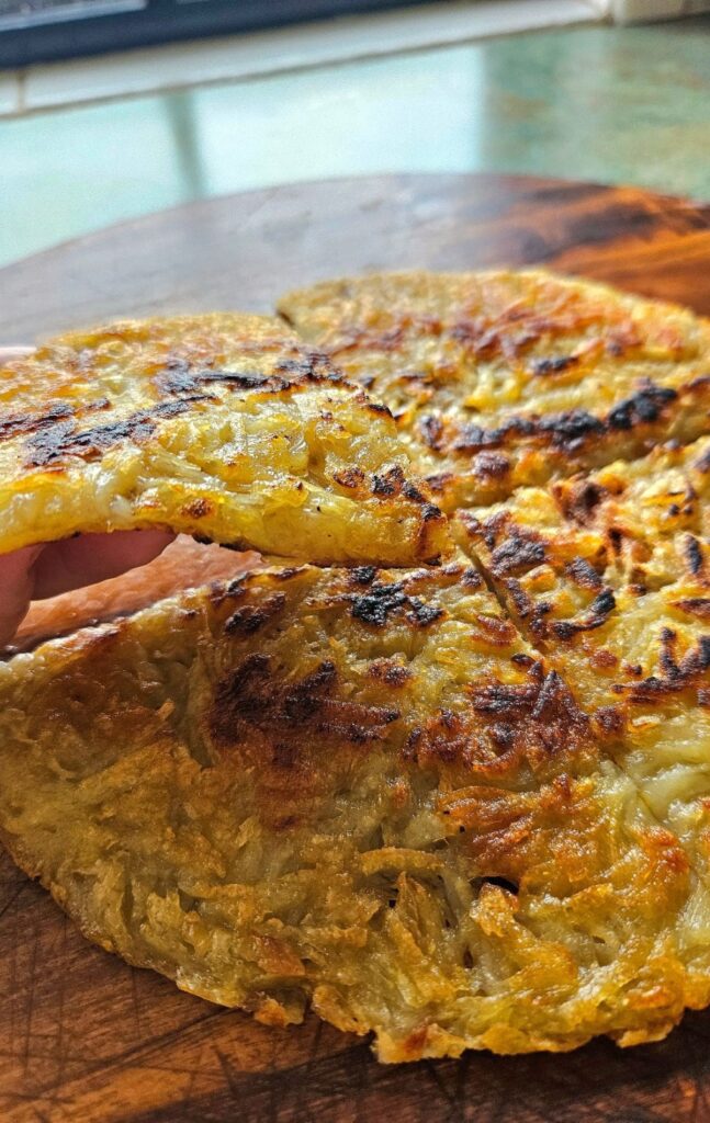 Crispy hashbrown sliced on a cutting board and a piece being held.