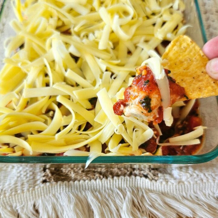 Layered bean dip in an container with a corn chip.