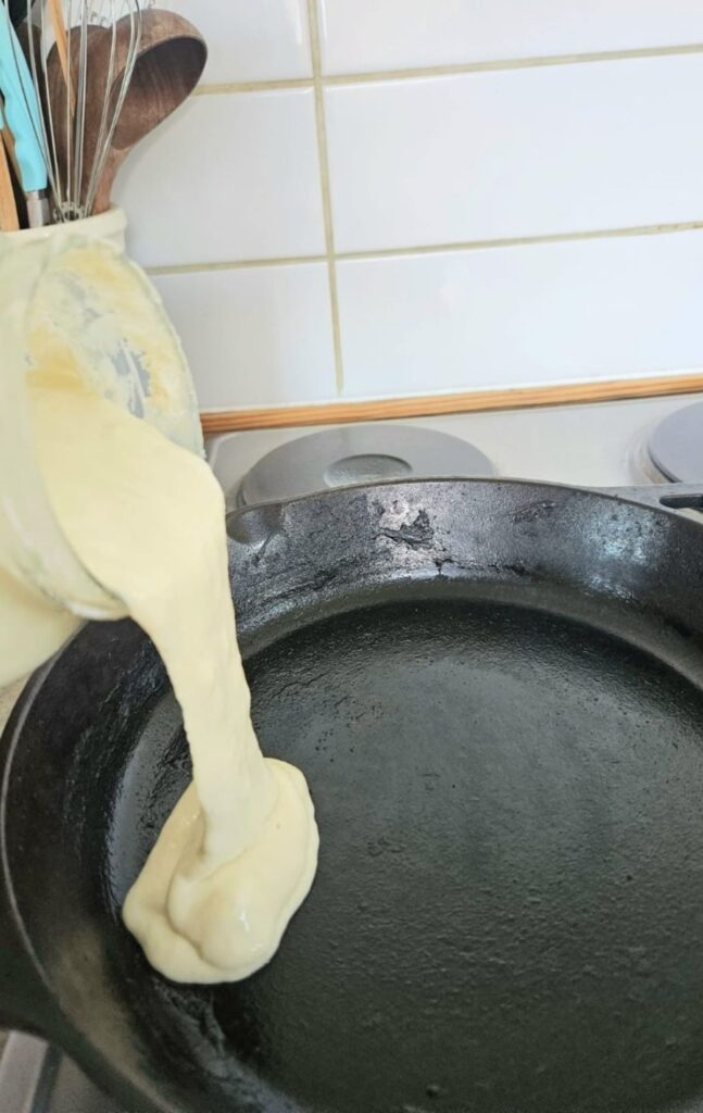 Pouring sourdough discard into hot cast iron pan.