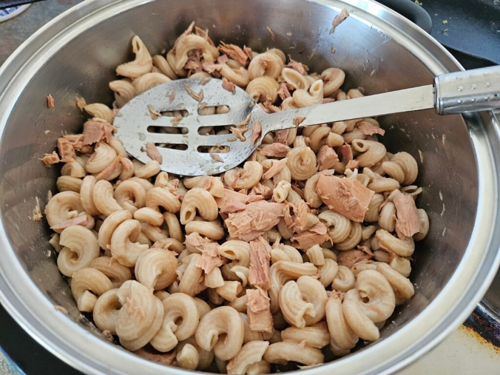 Adding tuna to cooked pasta in a large pot.