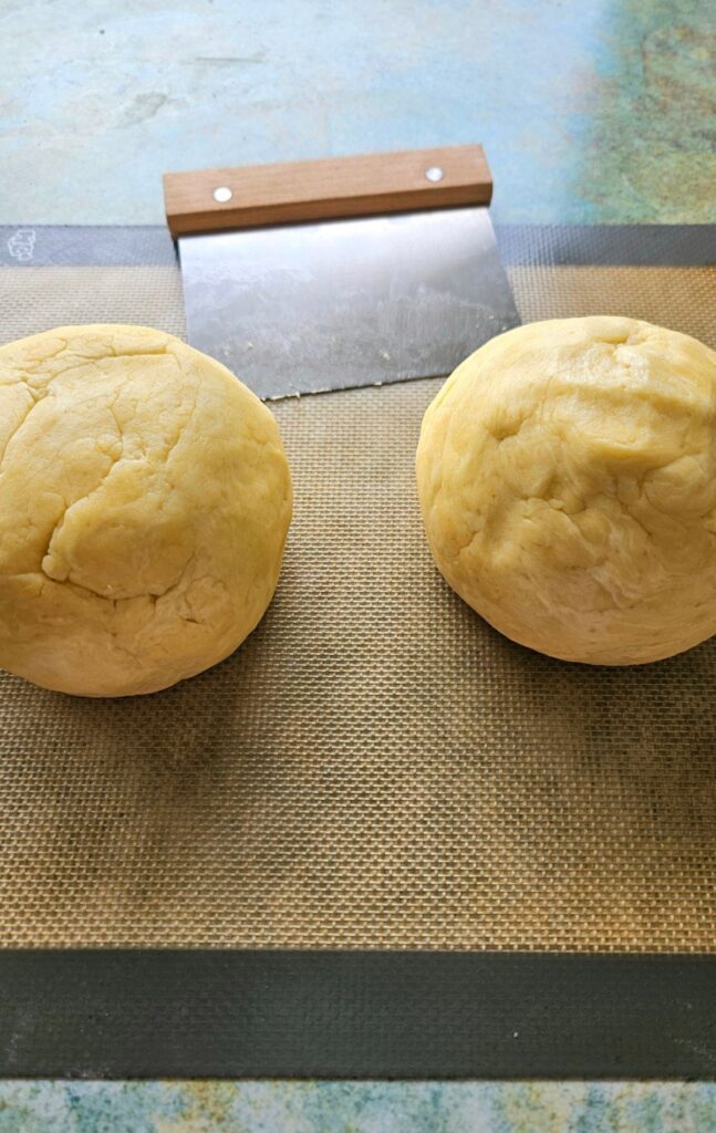 Two pie crust balls ready to be rolled out on a silicone mat.